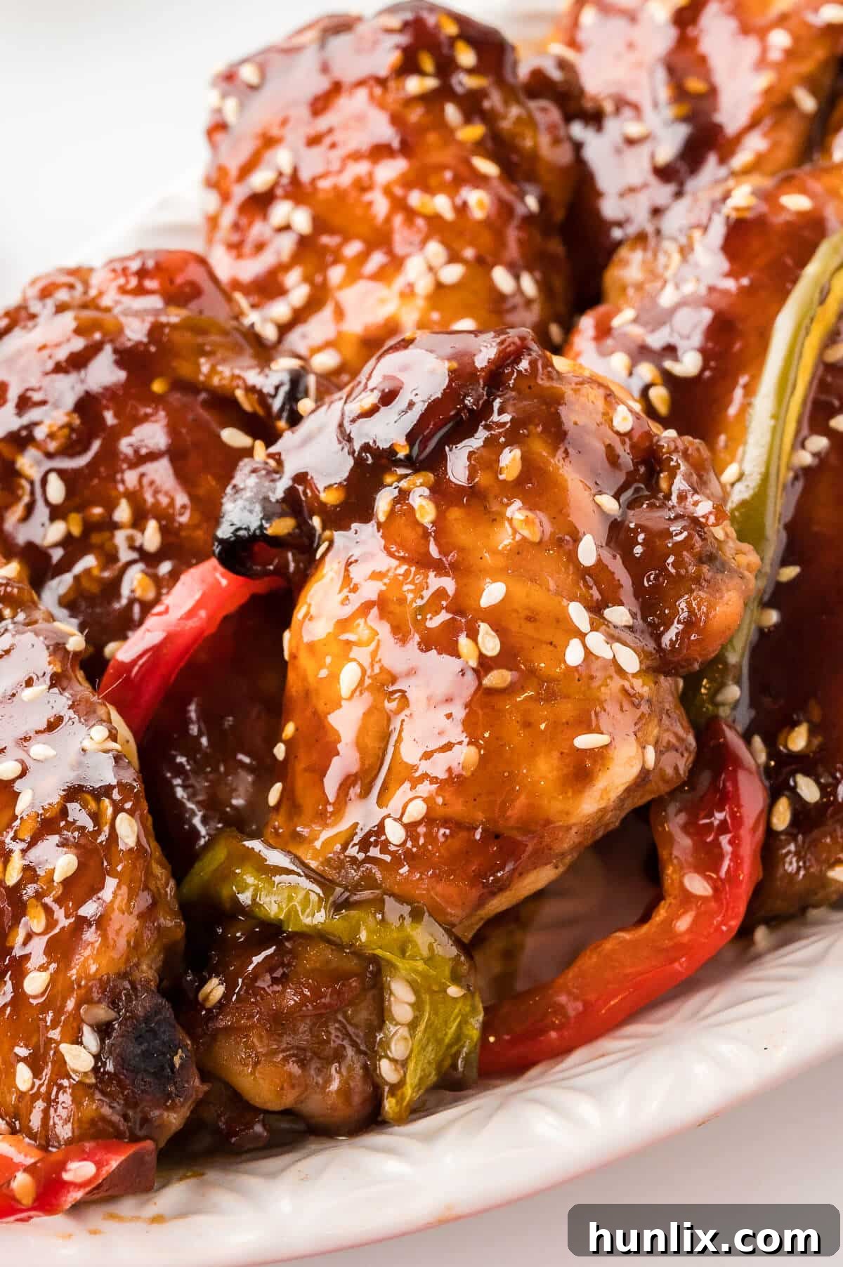 A serving platter overflowing with cooked Asian chicken wings, garnished with fresh sesame seeds and thinly sliced green and red bell peppers, highlighting their glistening glaze.