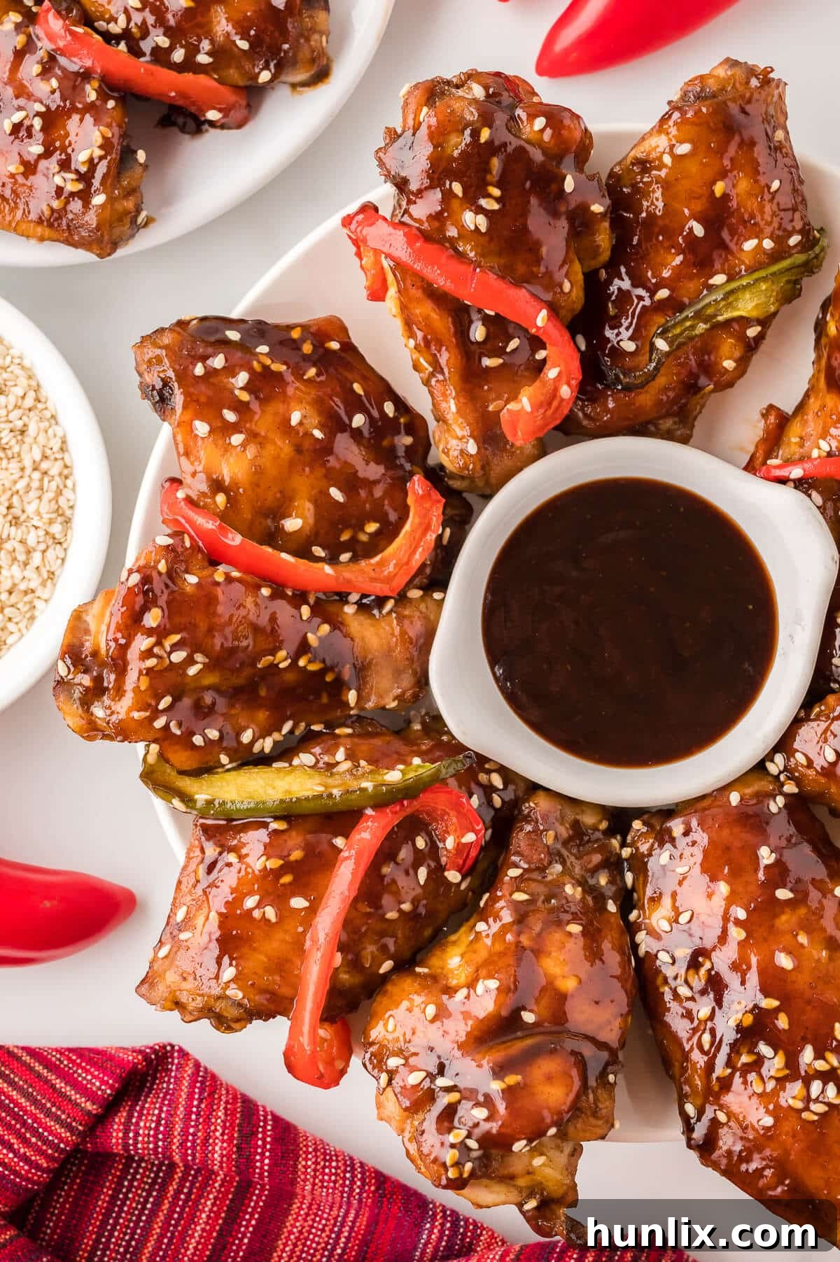 A platter of cooked Asian chicken wings served with a small bowl of dipping sauce, garnished with fresh green onions and bell pepper strips.