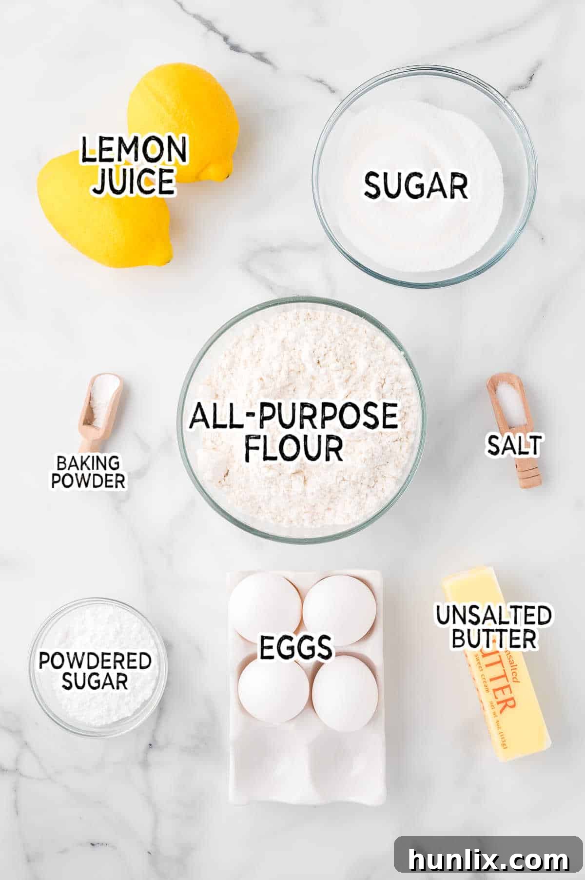 Ingredients for lemon bars laid out on a white marble background, including lemons, eggs, flour, sugar, and butter.