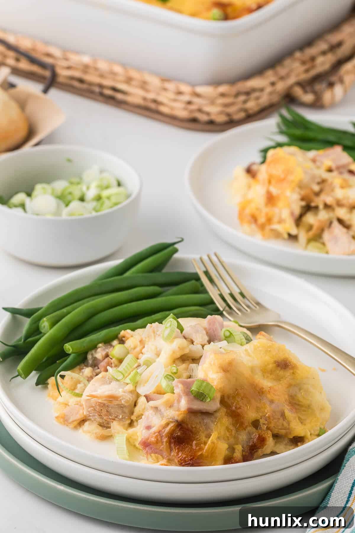 A close-up shot of a plate with chicken cordon bleu casserole, green beans, and a fork, emphasizing the rich, creamy texture and delicious layers.
