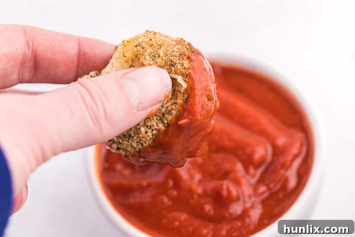 A hand dipping an air fryer mozzarella ball into pizza sauce.