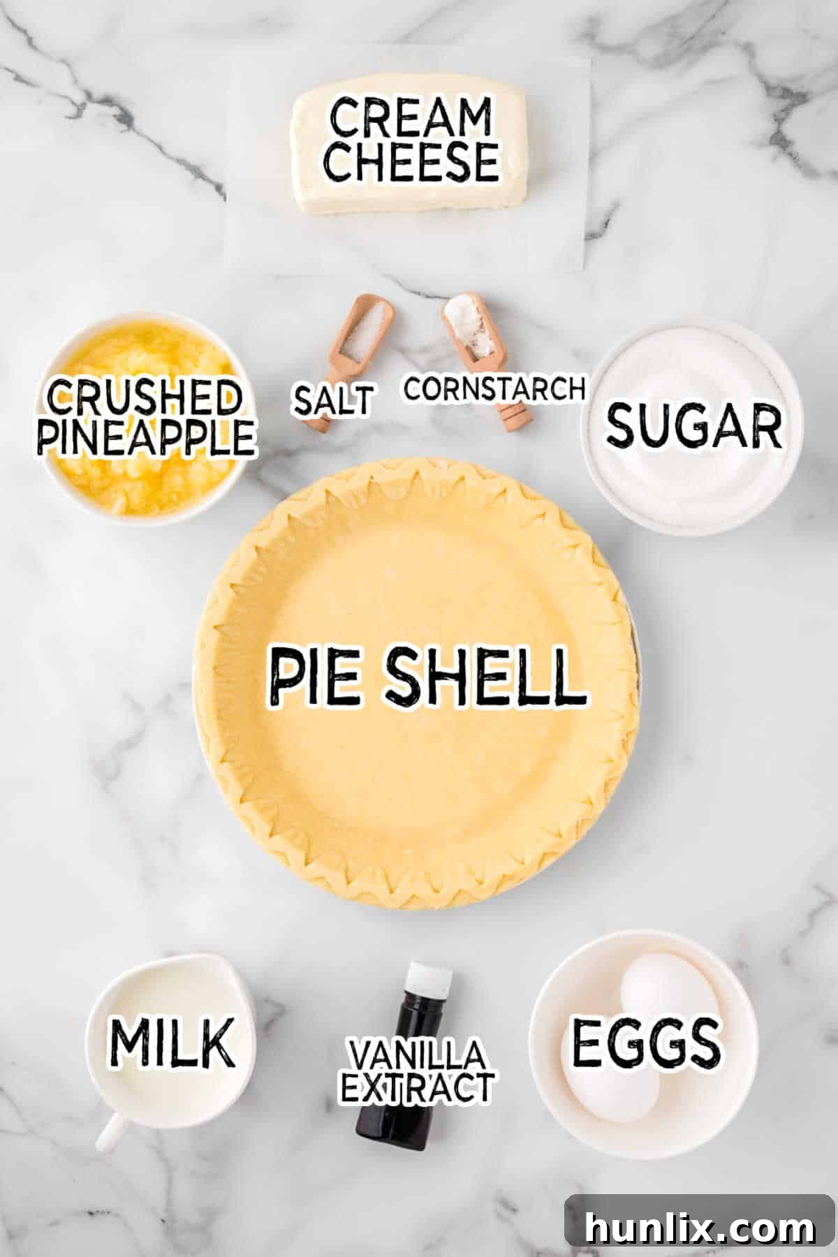 A collection of fresh and packaged ingredients, including cream cheese, sugar, eggs, and pineapple, neatly arranged on a marble counter.