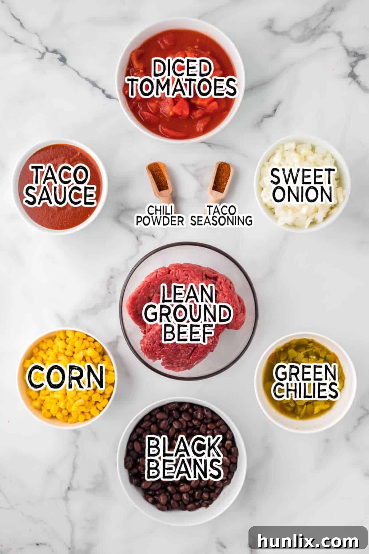 Ingredients laid out on a counter to make taco chili, including canned goods, ground beef, and onions.