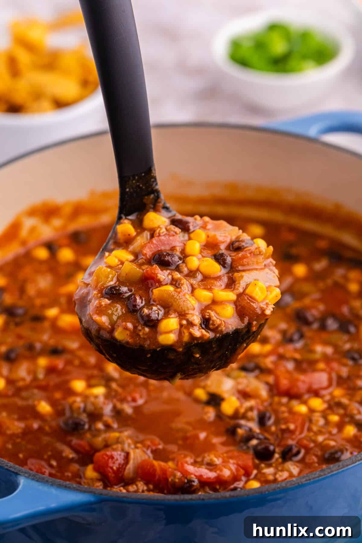 Taco chili being served from a pot with a black ladle, showcasing its rich texture.