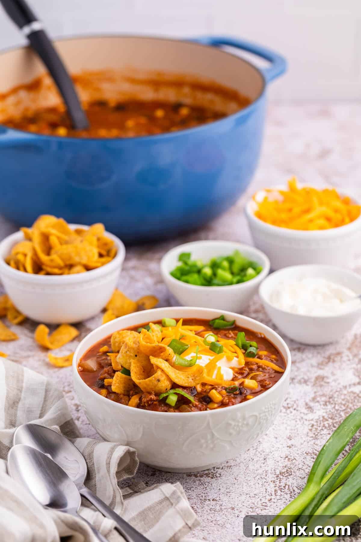 A close-up of taco chili in a white bowl with melted cheese, a dollop of sour cream, and chopped green onions.