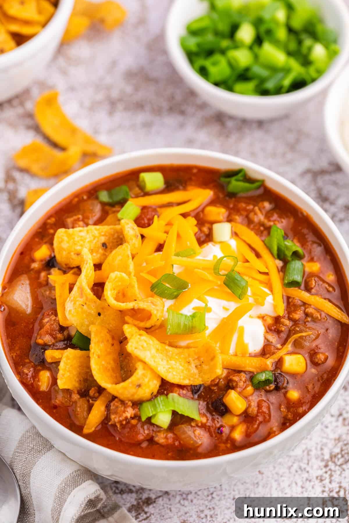 A bowl of taco chili with various toppings, including sour cream, cheese, and green onions, ready to eat.