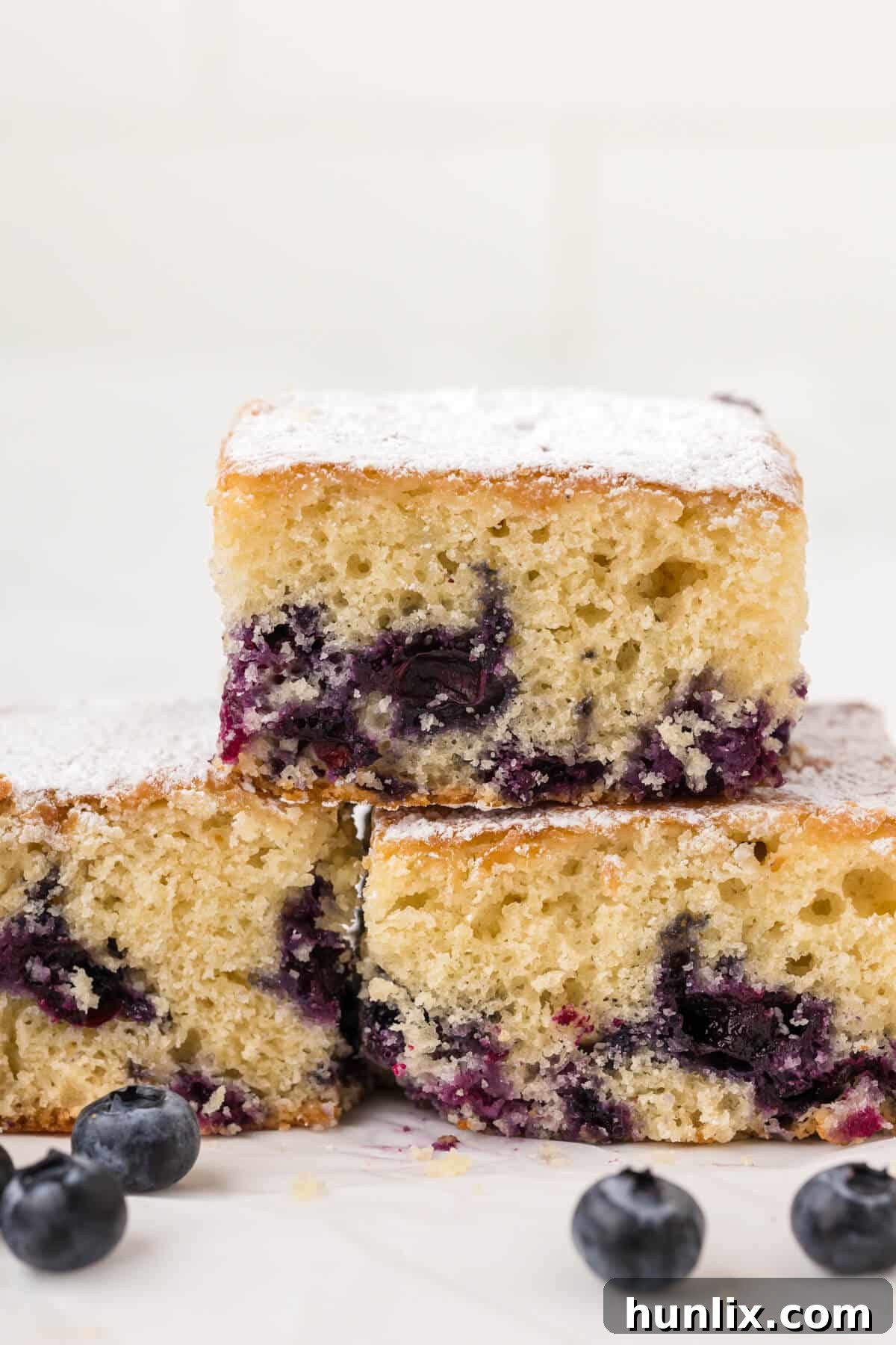A stack of golden-brown Blueberry Tea Cake slices on a white plate, showing the tender interior.