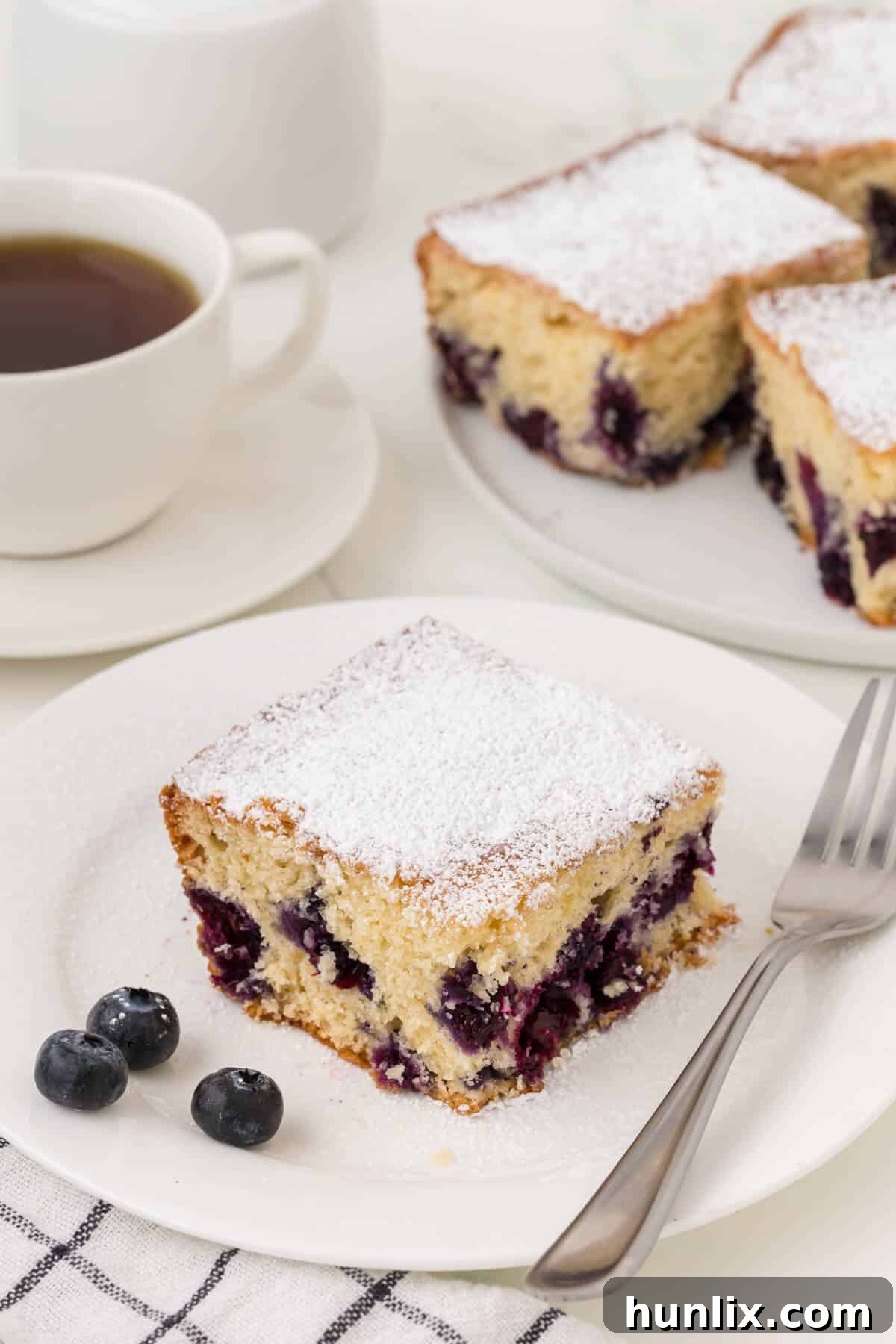 A single slice of Blueberry Tea Cake on a white plate with a fork, ready to be eaten.