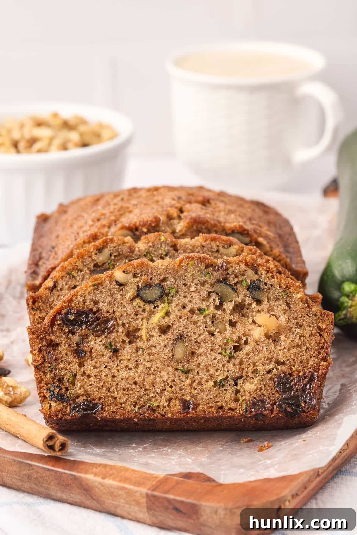 Slices cut off a loaf of zucchini bread, showcasing its moist texture with visible bits of zucchini, raisins, and walnuts.