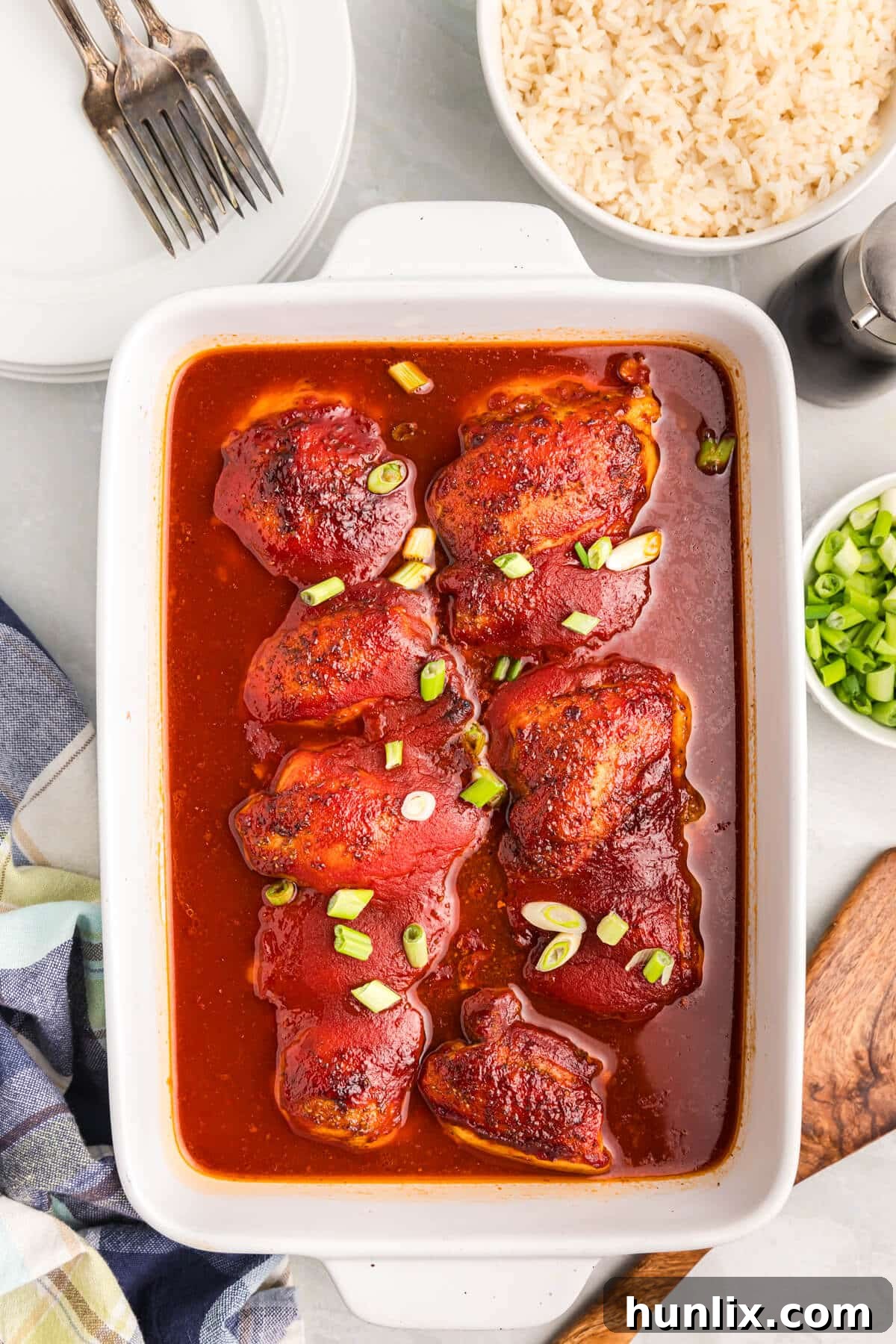 Delicious sweet and sour chicken thighs served in a ceramic casserole dish, garnished with fresh green onions and sesame seeds, ready to be enjoyed.