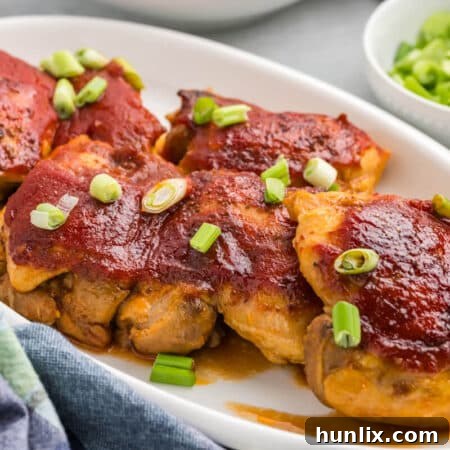 A top-down view of a round baking dish filled with sweet and sour chicken, garnished with fresh green onions and sesame seeds.