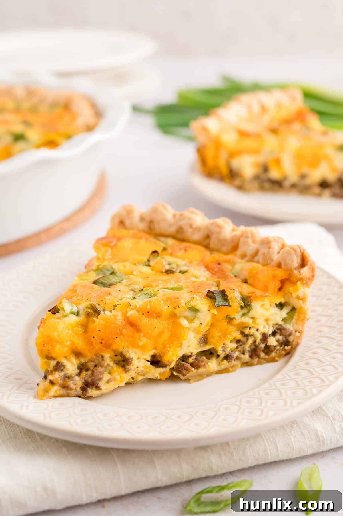 A beautiful slice of hamburger quiche served on a white plate with a fork.