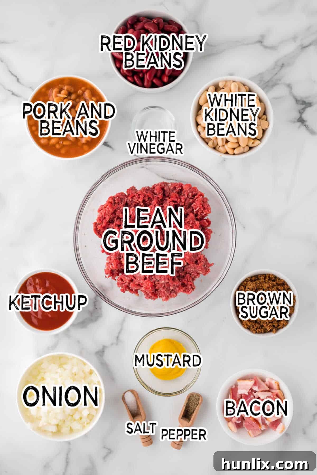 Various ingredients for baked bean casserole laid out on a marble countertop.