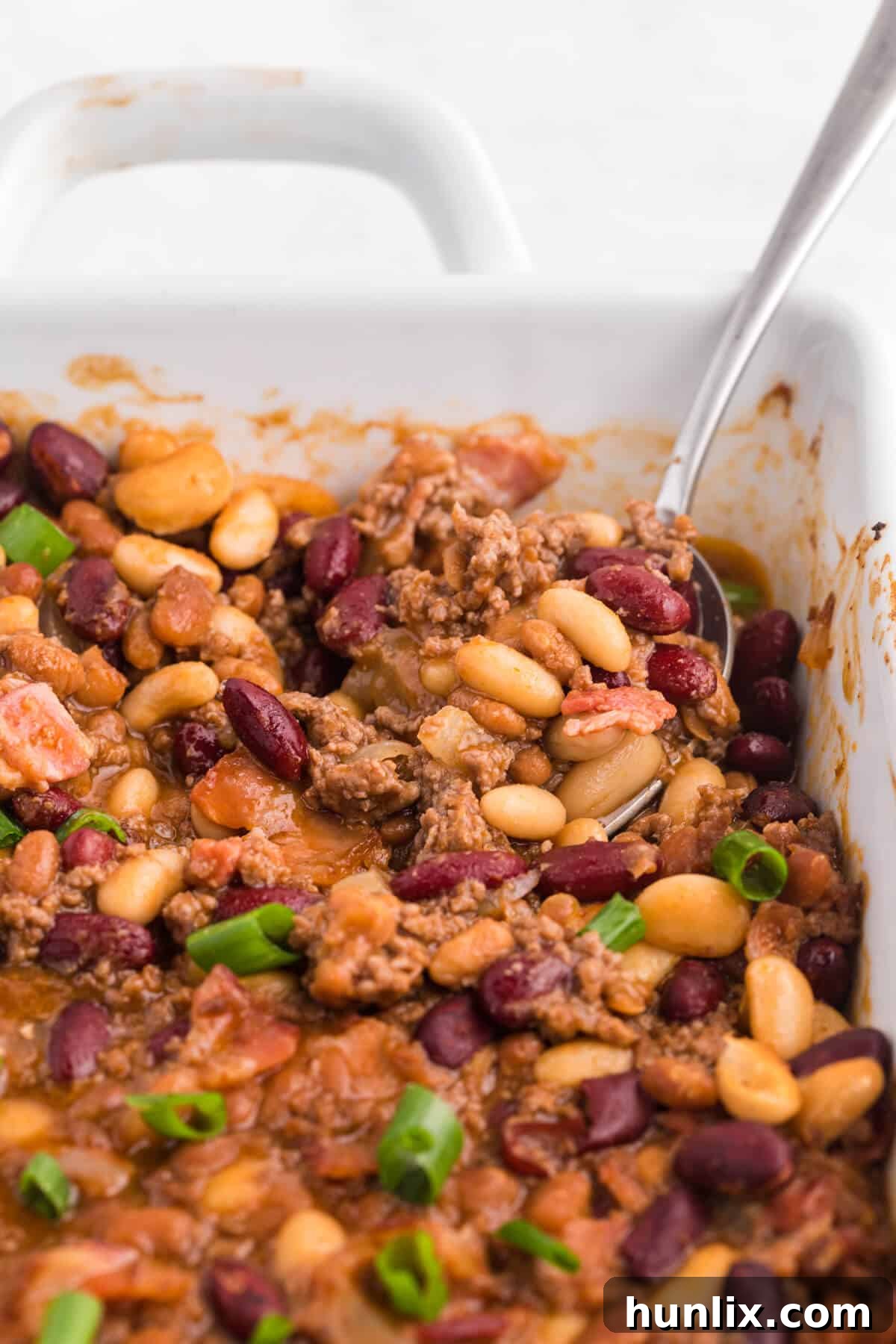 A close-up of the baked bean casserole in a pan with a serving spoon, highlighting its rich texture.