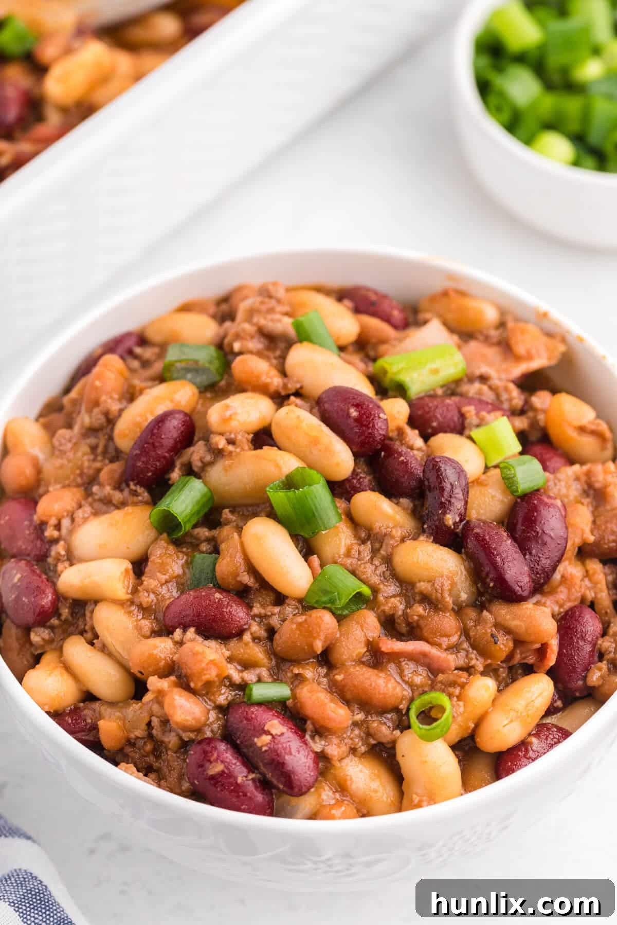 A baked bean casserole served in a white bowl, garnished with fresh green onions.