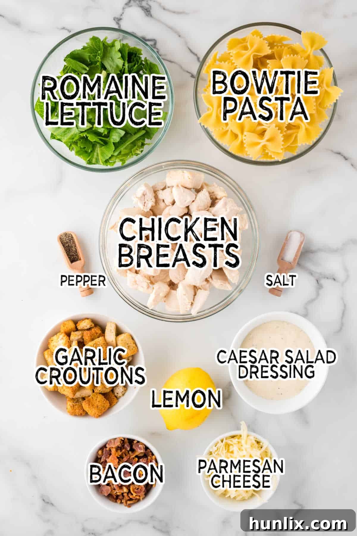 Signature Chicken Caesar Pasta 3 All the fresh ingredients for Chicken Caesar Pasta Salad laid out on a clean white marble counter, showcasing their vibrant colors and textures.
