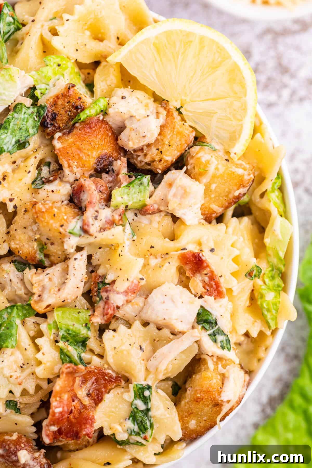 Signature Chicken Caesar Pasta 7 A close-up shot of the Chicken Caesar Pasta Salad, highlighting the varied textures of pasta, chicken, lettuce, bacon, and croutons, all coated in creamy dressing.