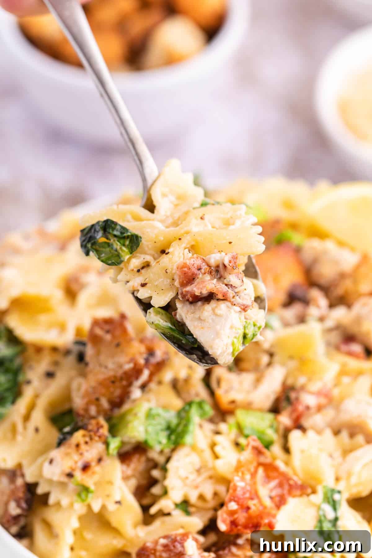 Signature Chicken Caesar Pasta 8 A spoonful of Chicken Caesar Pasta Salad, showcasing the perfect blend of pasta, chicken, and other ingredients, ready to be eaten.