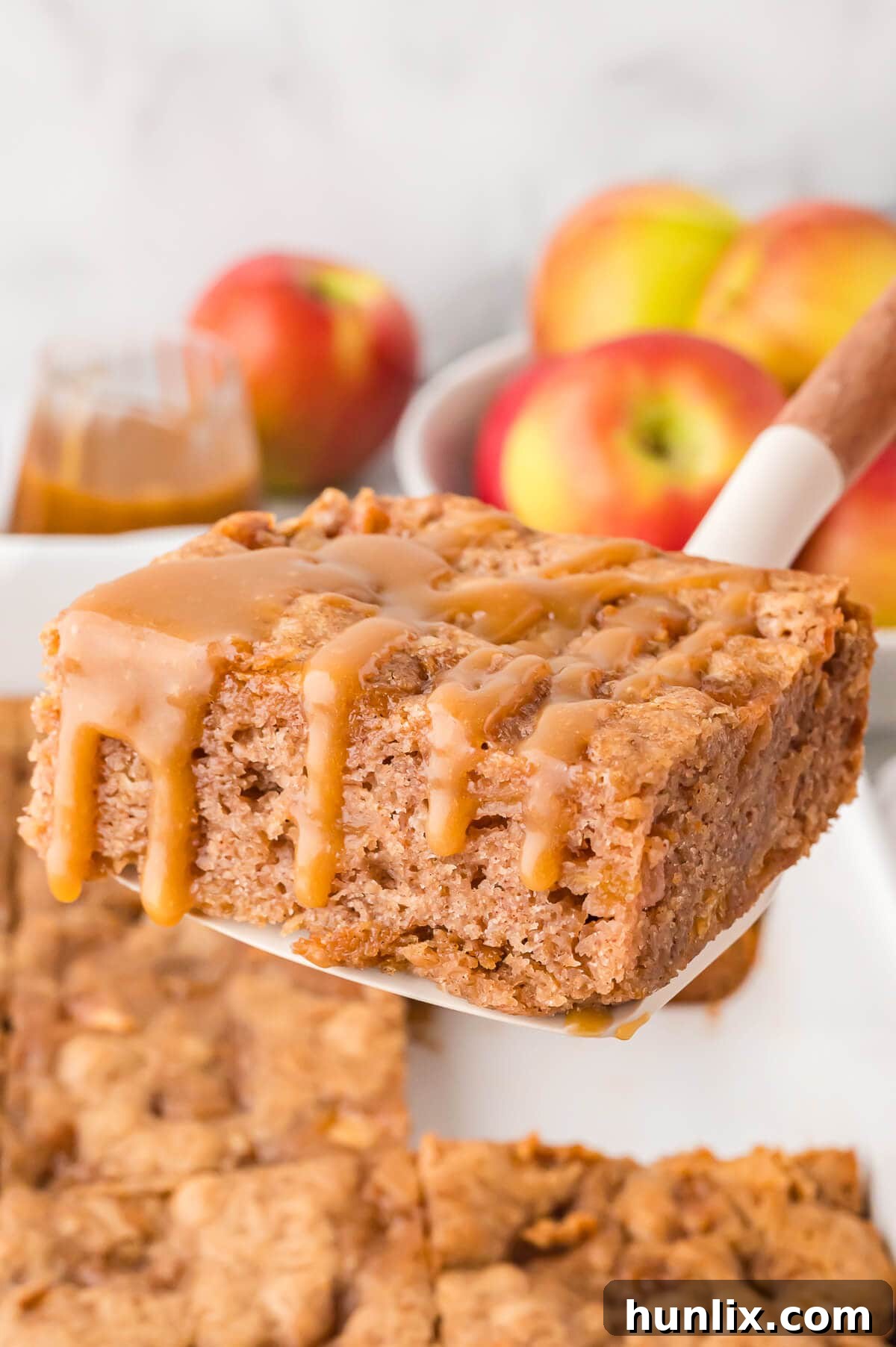 A perfectly sliced piece of moist apple cake, generously drizzled with golden butterscotch sauce, resting on a serving spatula, ready to be enjoyed.