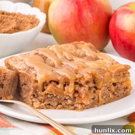 A slice of apple cake on a plate with a fork.