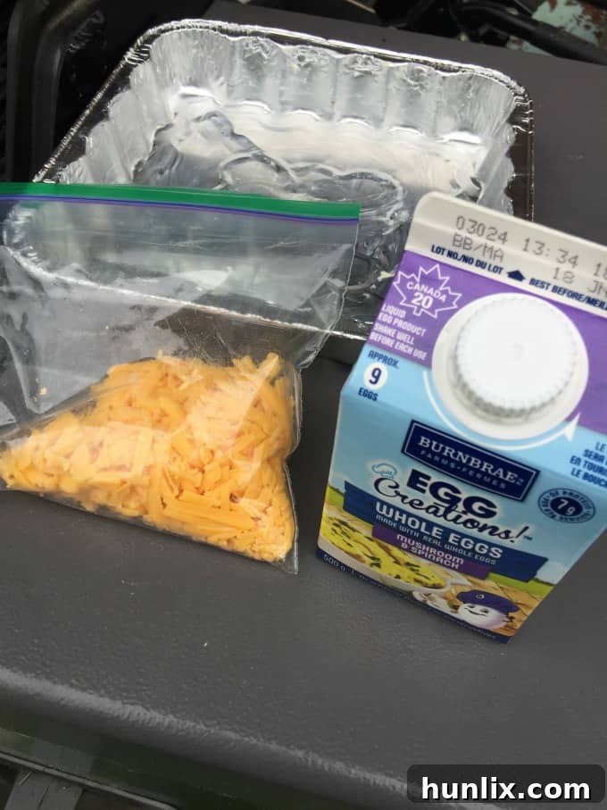 Close-up of golden, fluffy BBQ Eggs, generously garnished with fresh herbs and a sprinkle of black pepper, served steaming hot in a disposable foil pan. This image highlights a perfect, easy camping breakfast for outdoor enthusiasts.