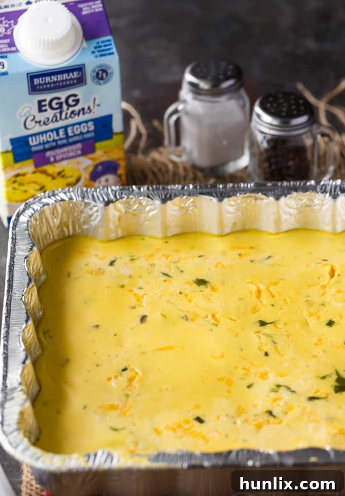 A person prepares a disposable foil pan of BBQ Eggs on a portable camping grill, set up amidst a scenic outdoor campsite, illustrating the practical application of this easy camping breakfast recipe.