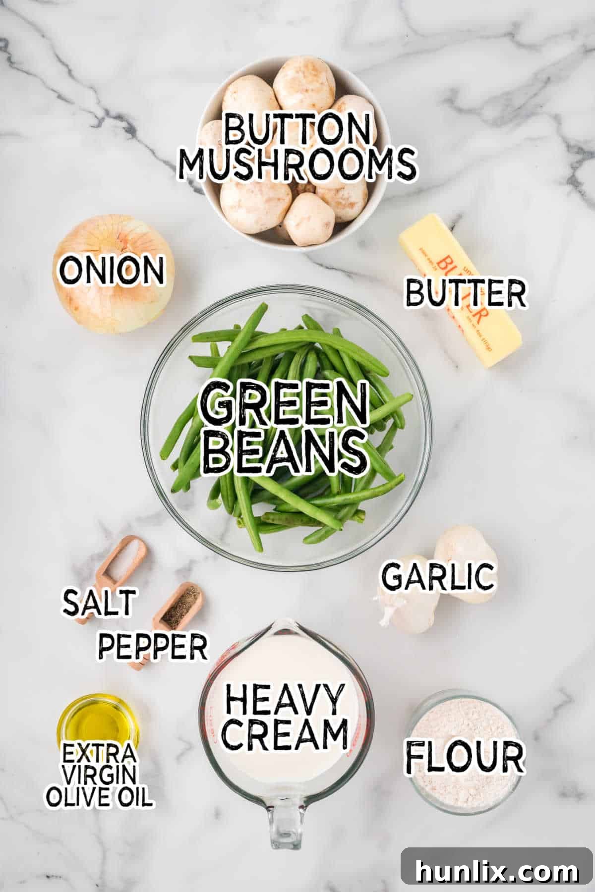 Homestyle Green Bean Bake 3 Various fresh ingredients for green bean casserole laid out on a white marble counter, including green beans, mushrooms, cream, and butter.