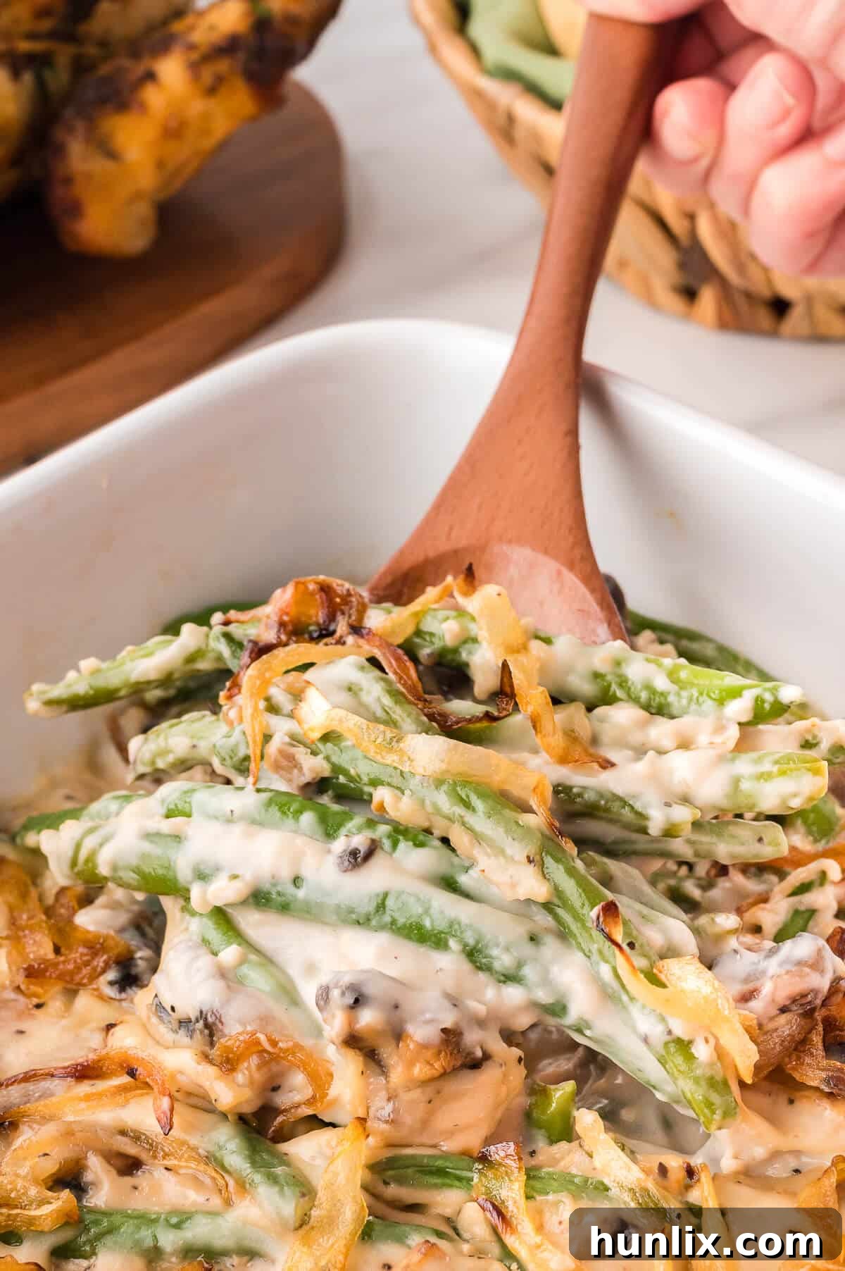 Homestyle Green Bean Bake 8 A close-up of green bean casserole with a wooden spoon taking a scoop, showcasing its texture and a generous topping.