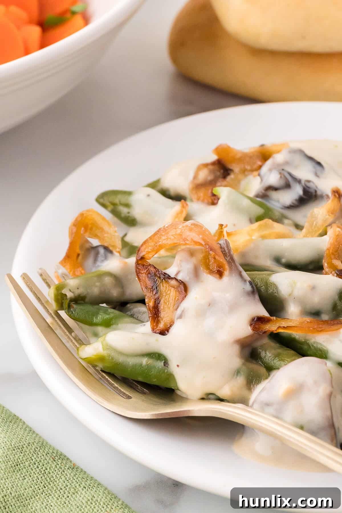 Homestyle Green Bean Bake 10 A serving of homemade green bean casserole on a white plate with a fork, showcasing its appealing texture and rich topping.