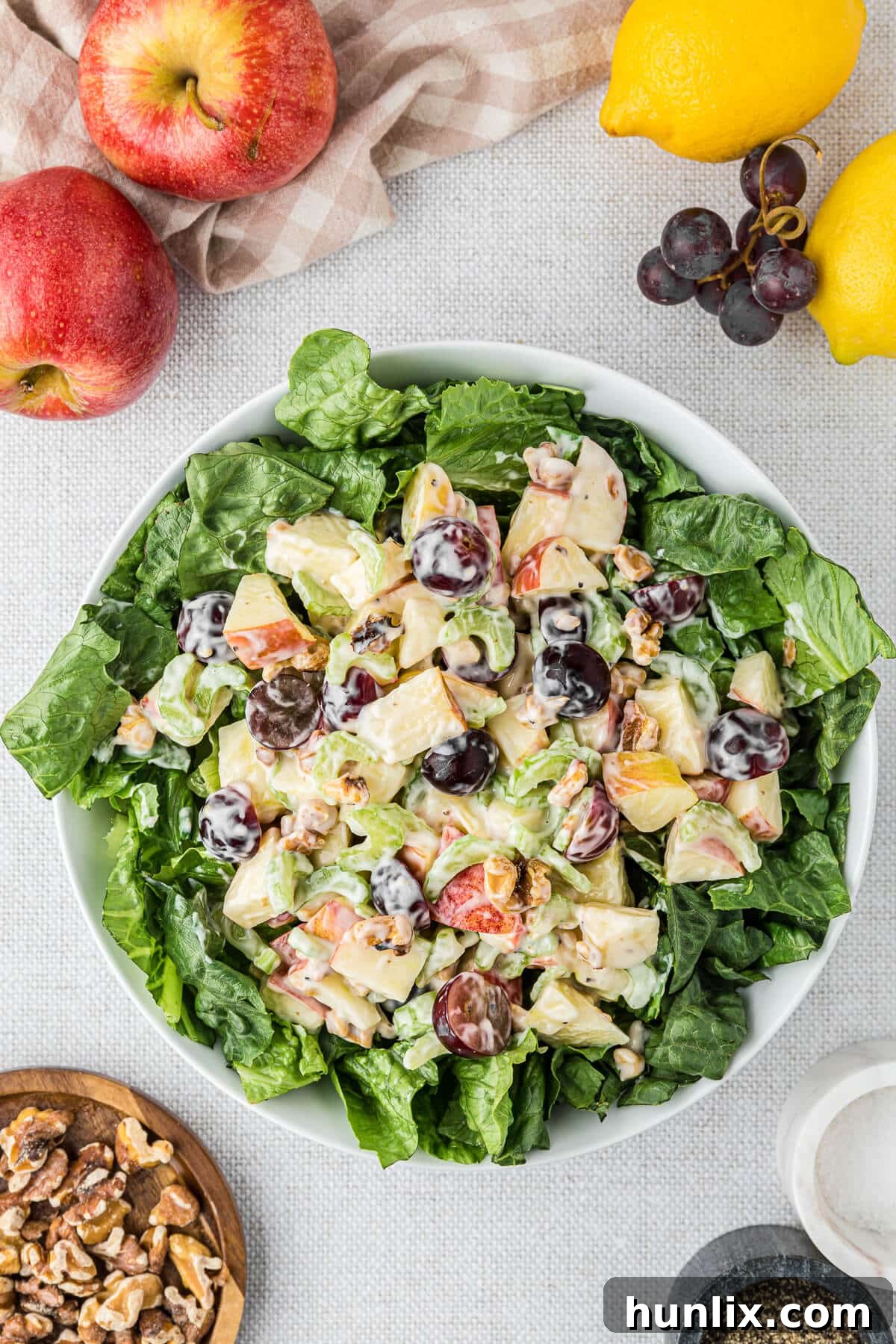 A vibrant bowl of Waldorf salad, generously portioned and ready to be enjoyed, surrounded by fresh ingredients like crisp green apples, juicy red grapes, crunchy walnuts, and celery stalks on a rustic wooden table.