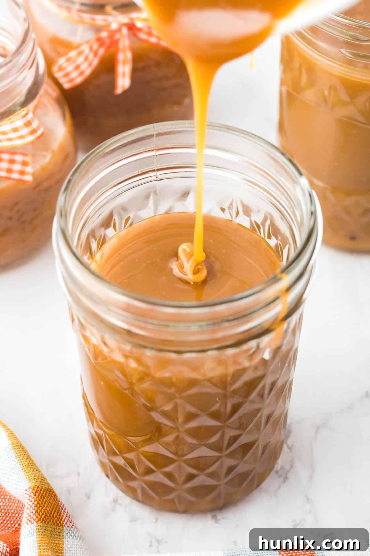 Homemade butterscotch sauce in a glass jar, with a spoon gently drizzling the golden sauce inside.