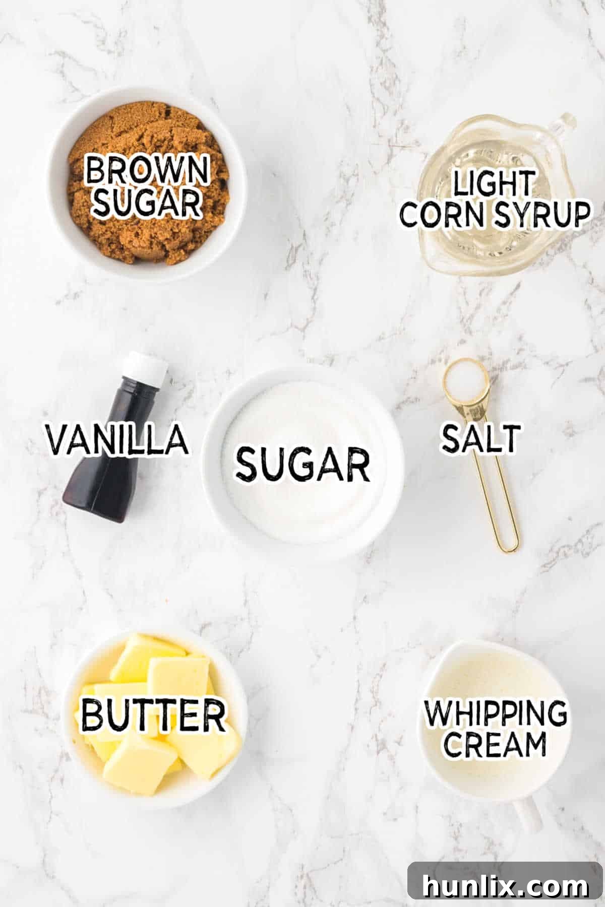 A collection of ingredients for butterscotch sauce, including sugars, butter, cream, and vanilla, neatly arranged on a marble countertop.