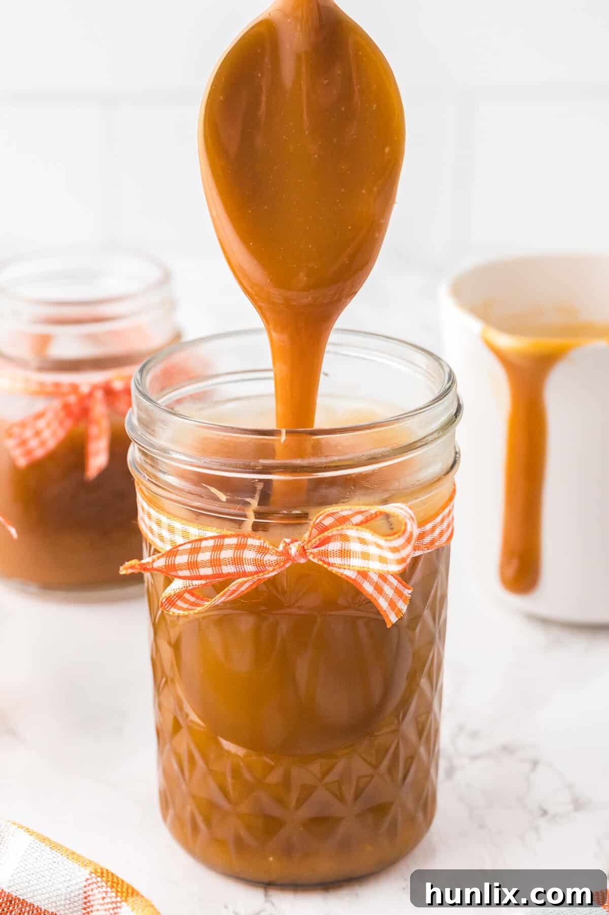 A spoon gently drizzling homemade butterscotch sauce into a glass jar, highlighting its rich, thick consistency.