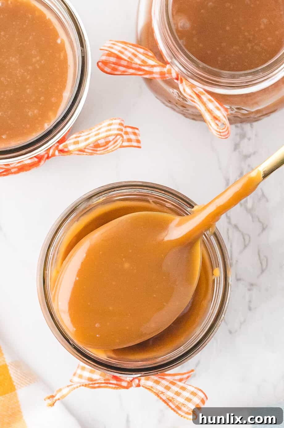 A spoon overflowing with rich butterscotch sauce, held above a glass jar filled with the golden confection.