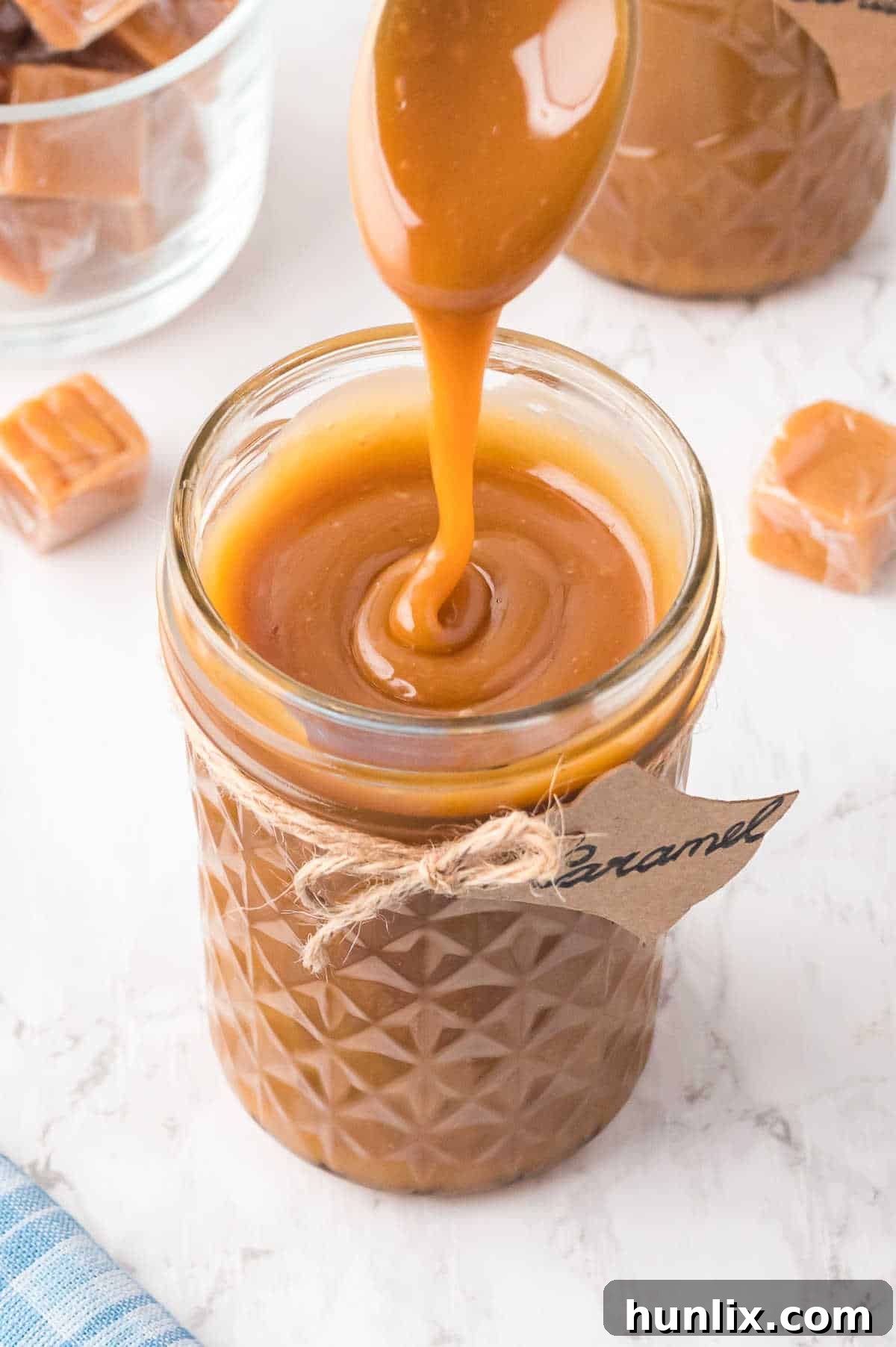 Caramel sauce being drizzled into a glass jar from a spoon, showcasing its smooth texture and rich amber color.