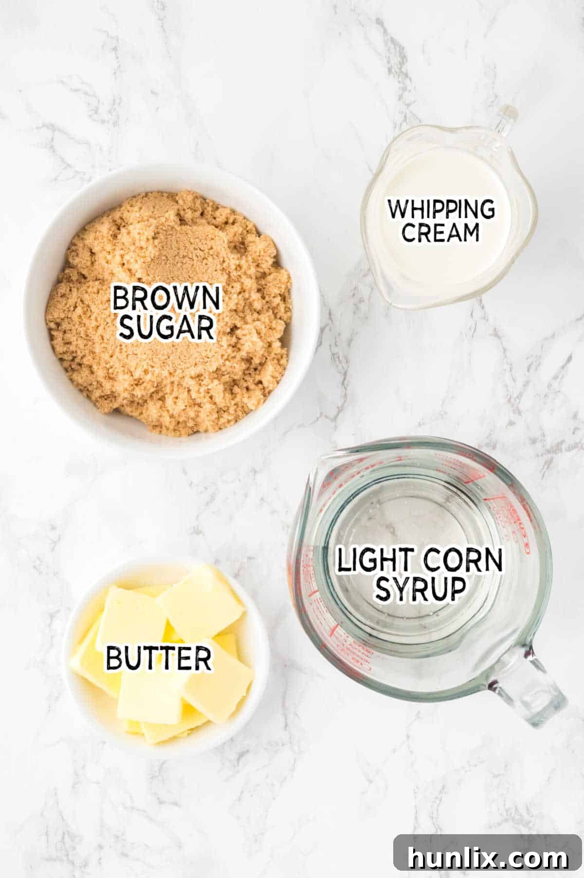 Ingredients for homemade caramel sauce, including corn syrup, brown sugar, butter, and heavy cream, laid out on a white marble surface.