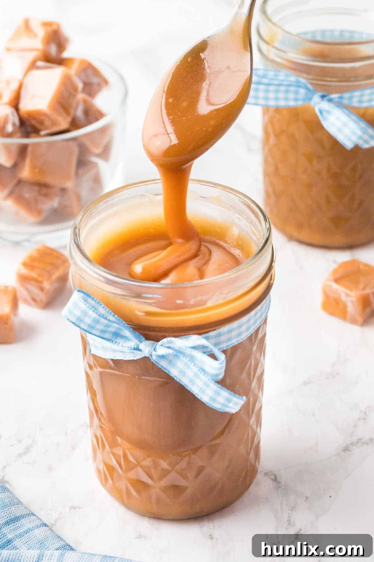 The finished homemade caramel sauce in a glass jar with a spoon, showing its thick and glossy texture.