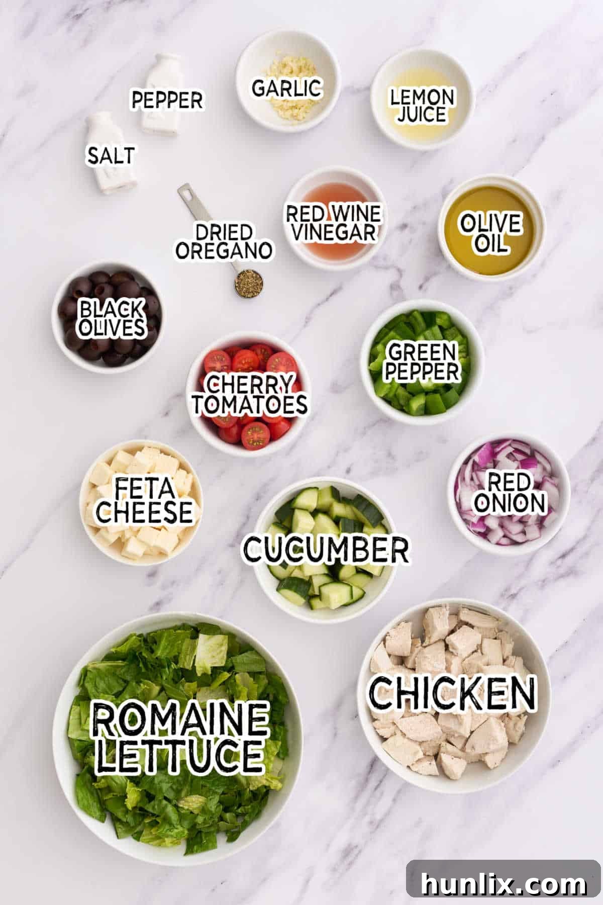 Assortment of fresh ingredients laid out on a white counter, ready to make Greek Chicken Salad.