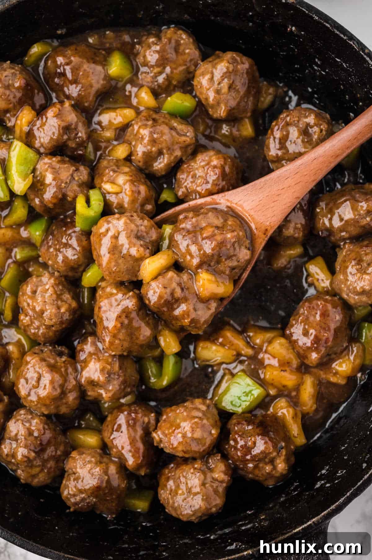 A wooden spoon scooping up a Waikiki meatball from a skillet, showcasing the rich sauce and pineapple tidbits.