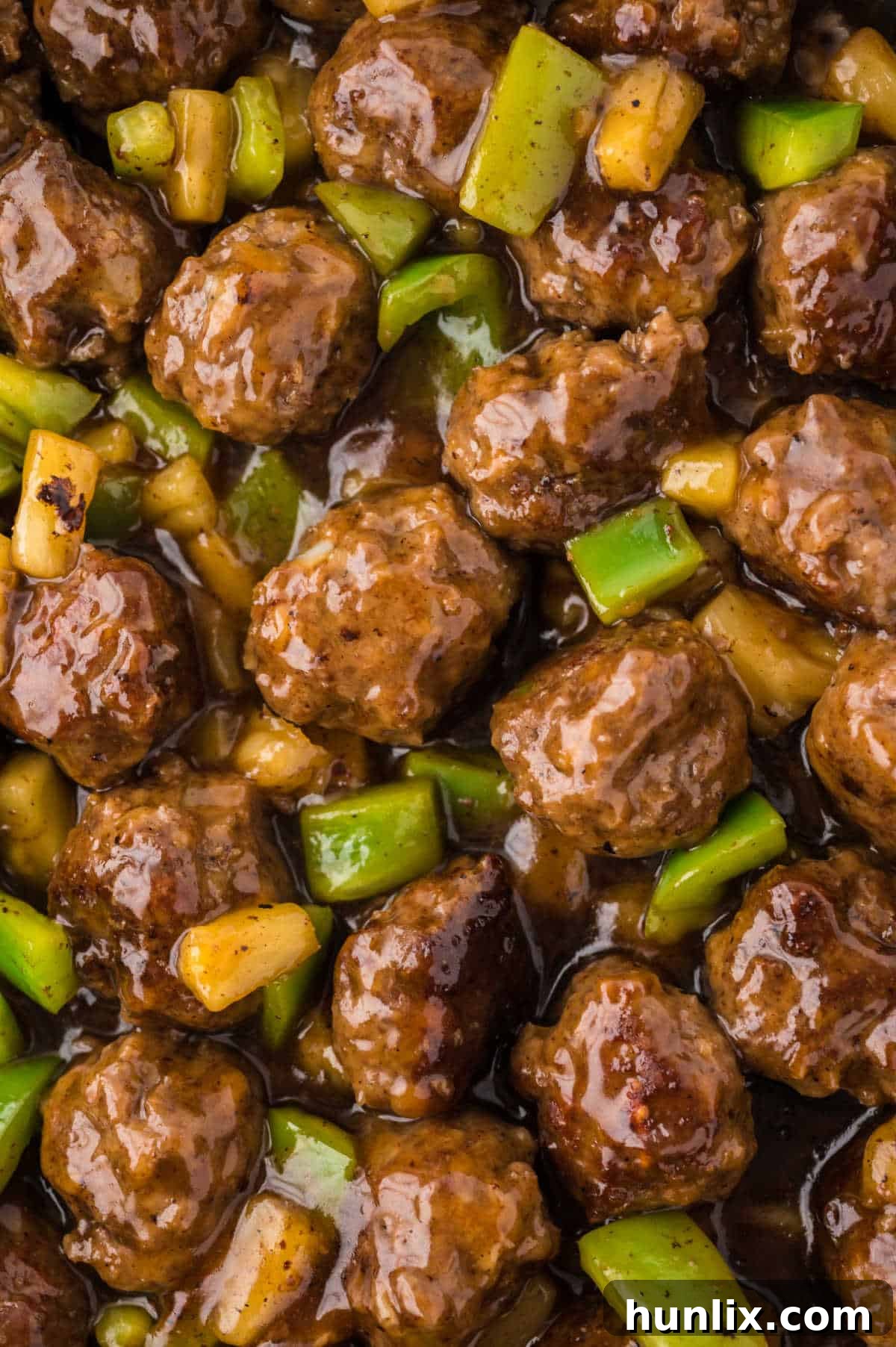A close-up view of Waikiki meatballs simmering in the sweet and sour sauce within a pan, highlighting the texture and color.