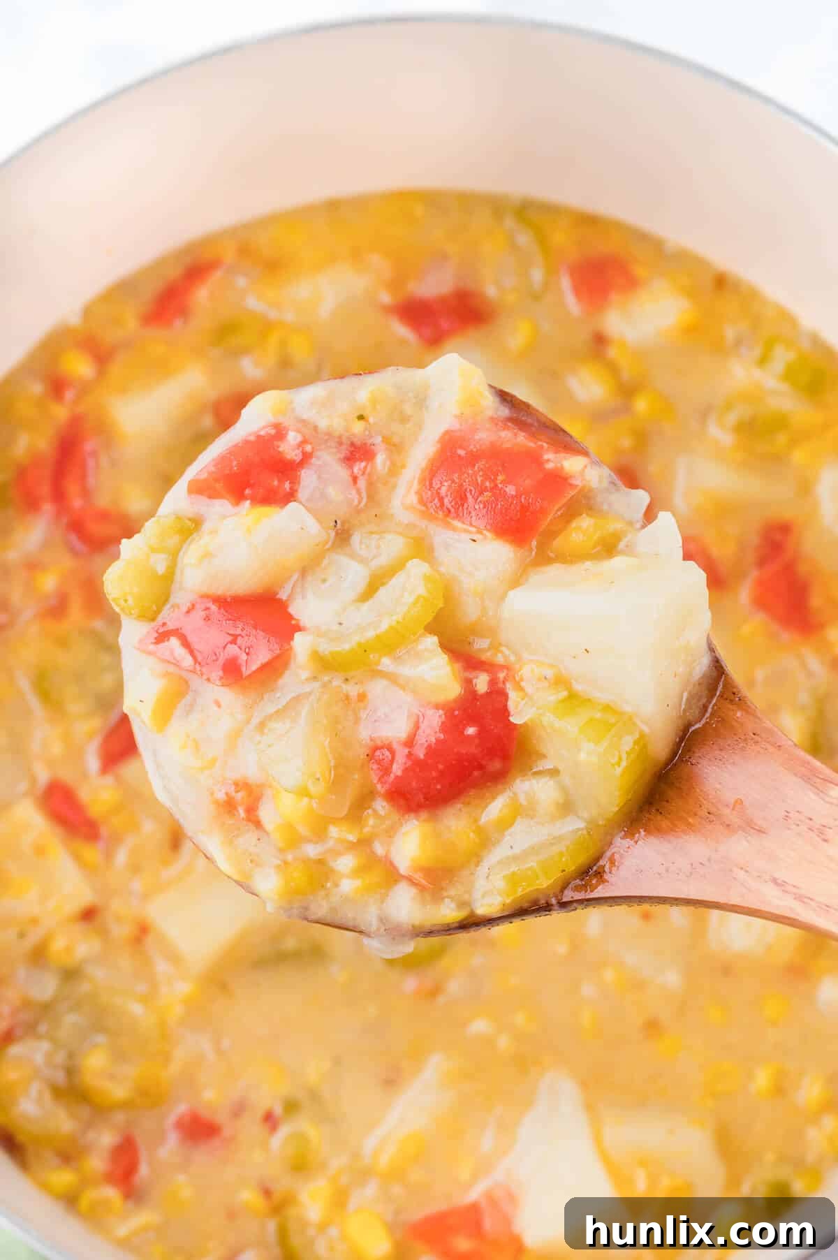 Sunshine Corn Chowder 7 A wooden ladle lifting a generous portion of creamy corn chowder from a pot, highlighting the rich texture and colorful ingredients, ready to be served into a bowl.