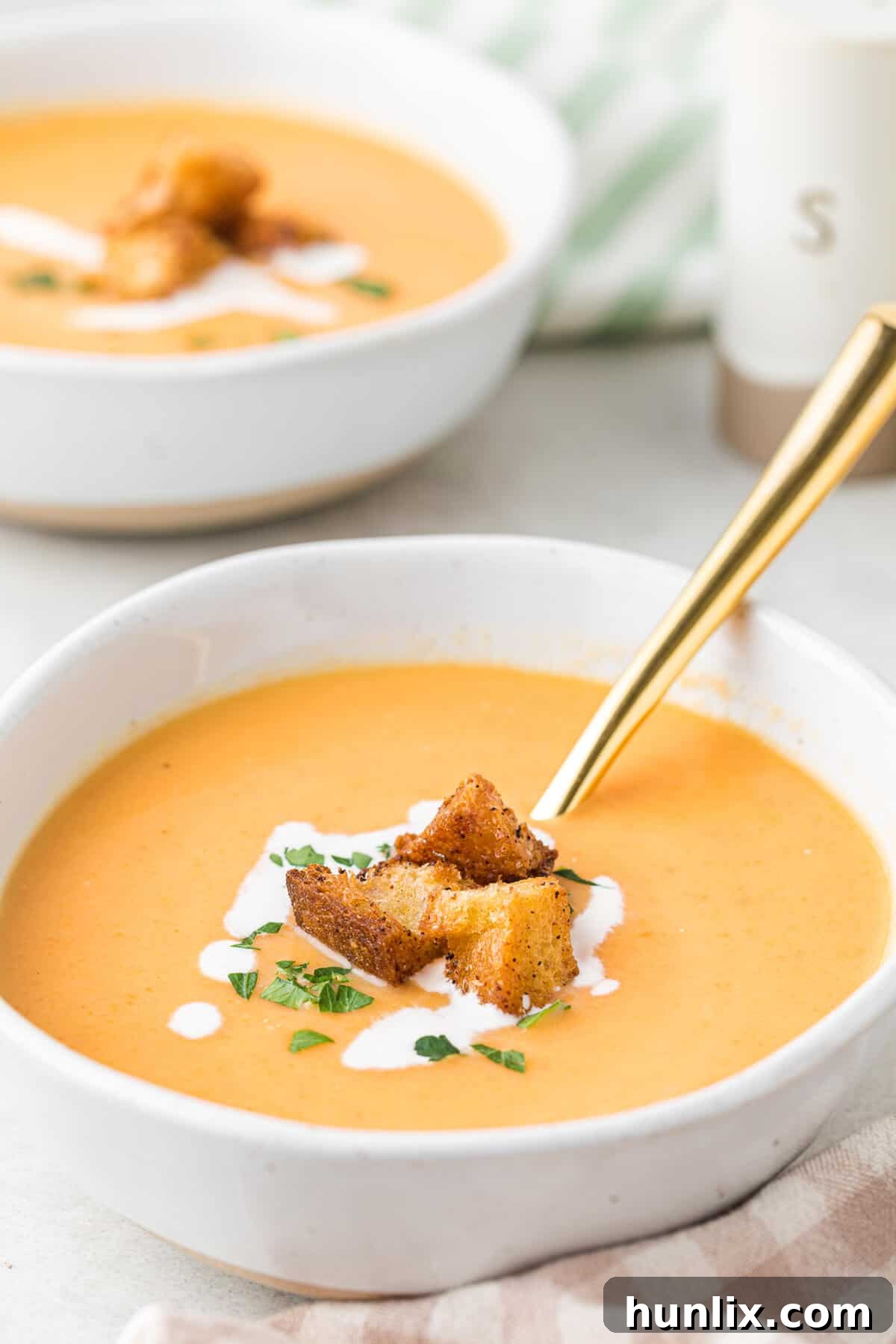A beautiful bowl of cream of carrot soup, garnished with crispy croutons, with a golden spoon resting in it.