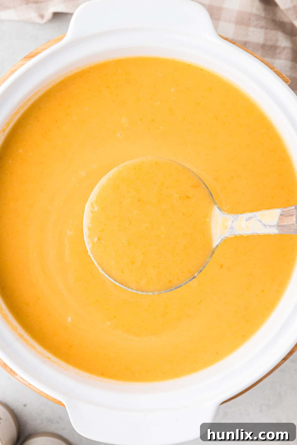 A large pot of cream of carrot soup being served with a ladle, showcasing its rich texture.
