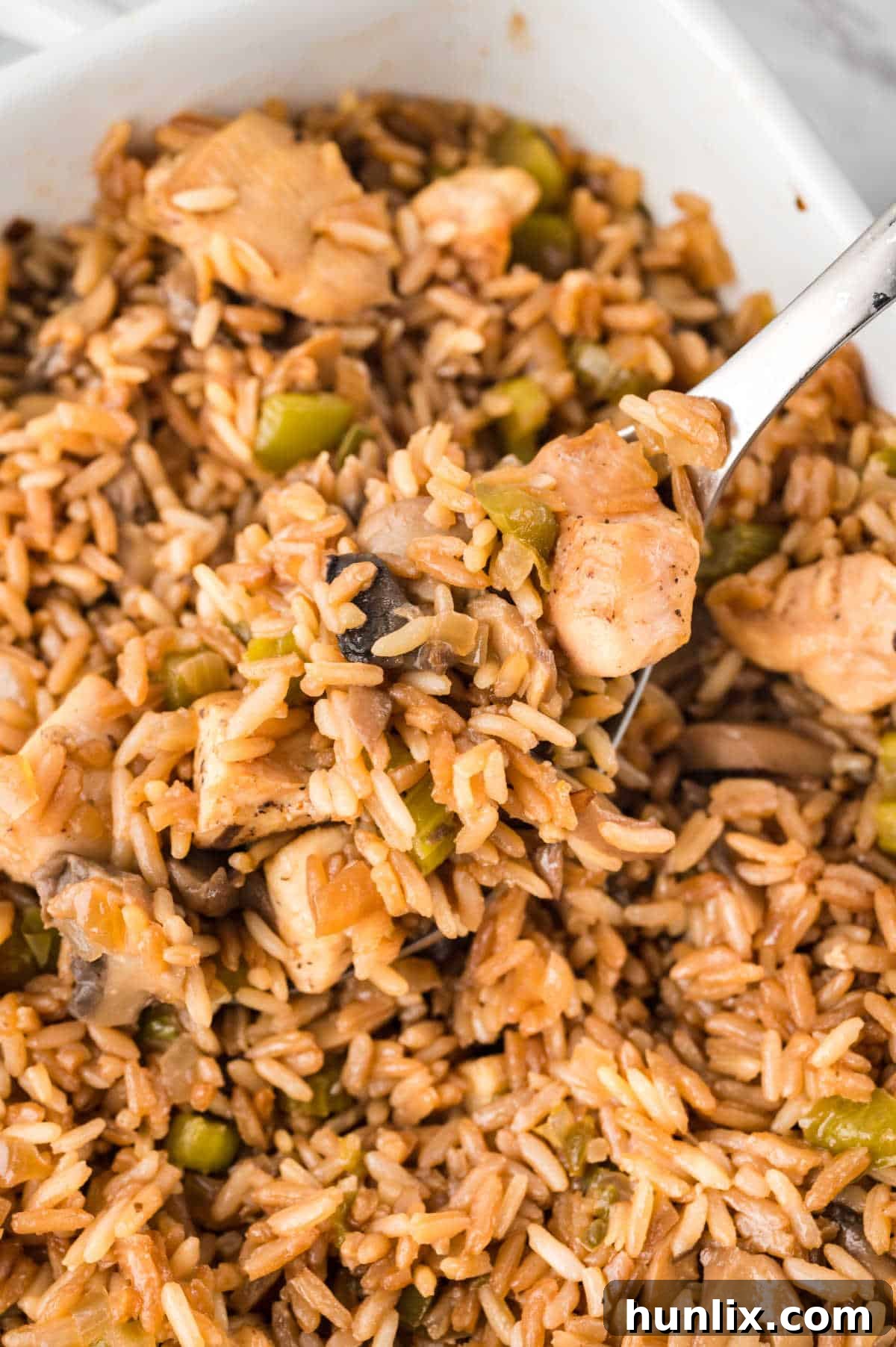 A casserole dish of chicken fried rice with a serving spoon, showcasing the fluffy rice, chicken, and vegetables.