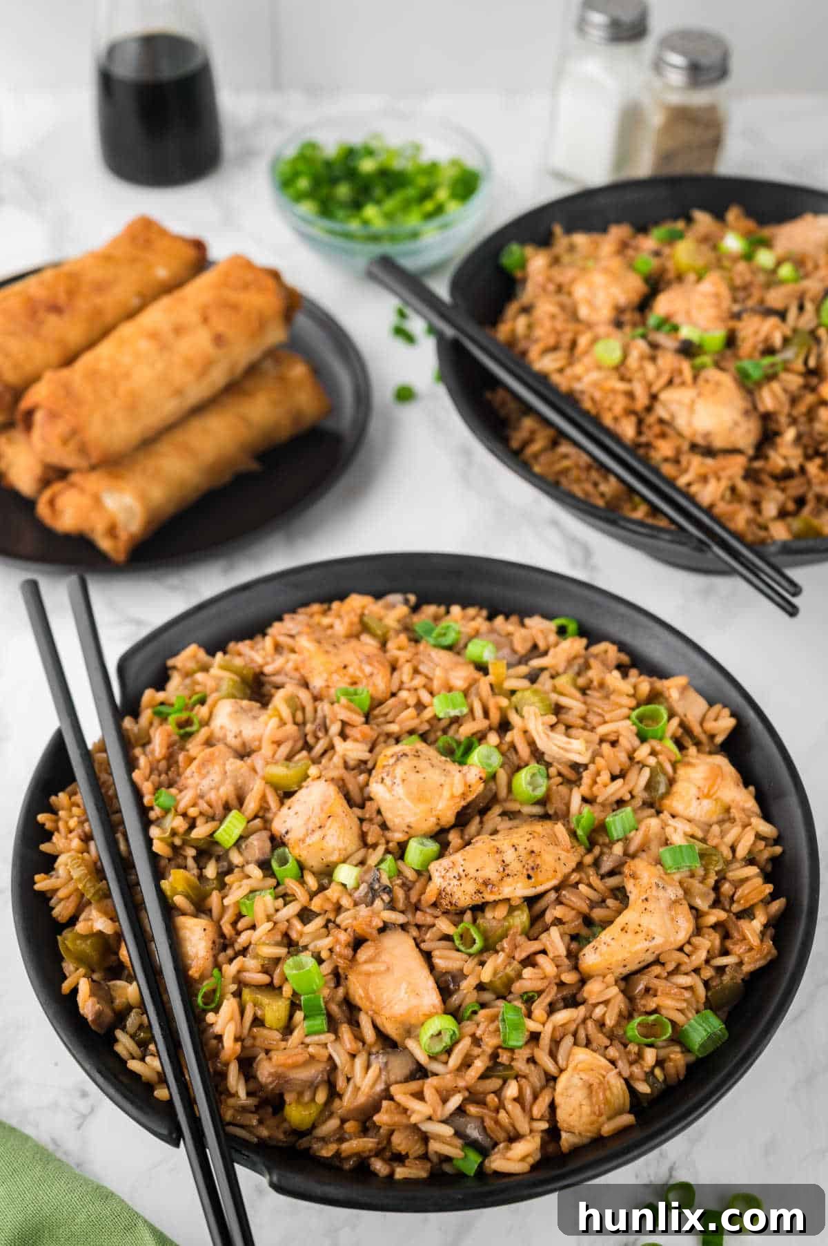 A black bowl brimming with freshly made chicken fried rice, garnished with green onions and ready to be enjoyed with chopsticks.