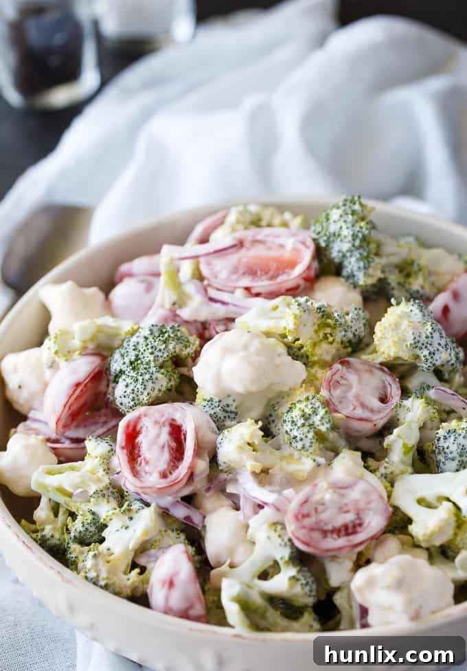 Yuletide Medley Salad 2 Vibrant Christmas Salad showcasing green broccoli, white cauliflower, red cherry tomatoes, and red onion, all coated in a creamy dressing.