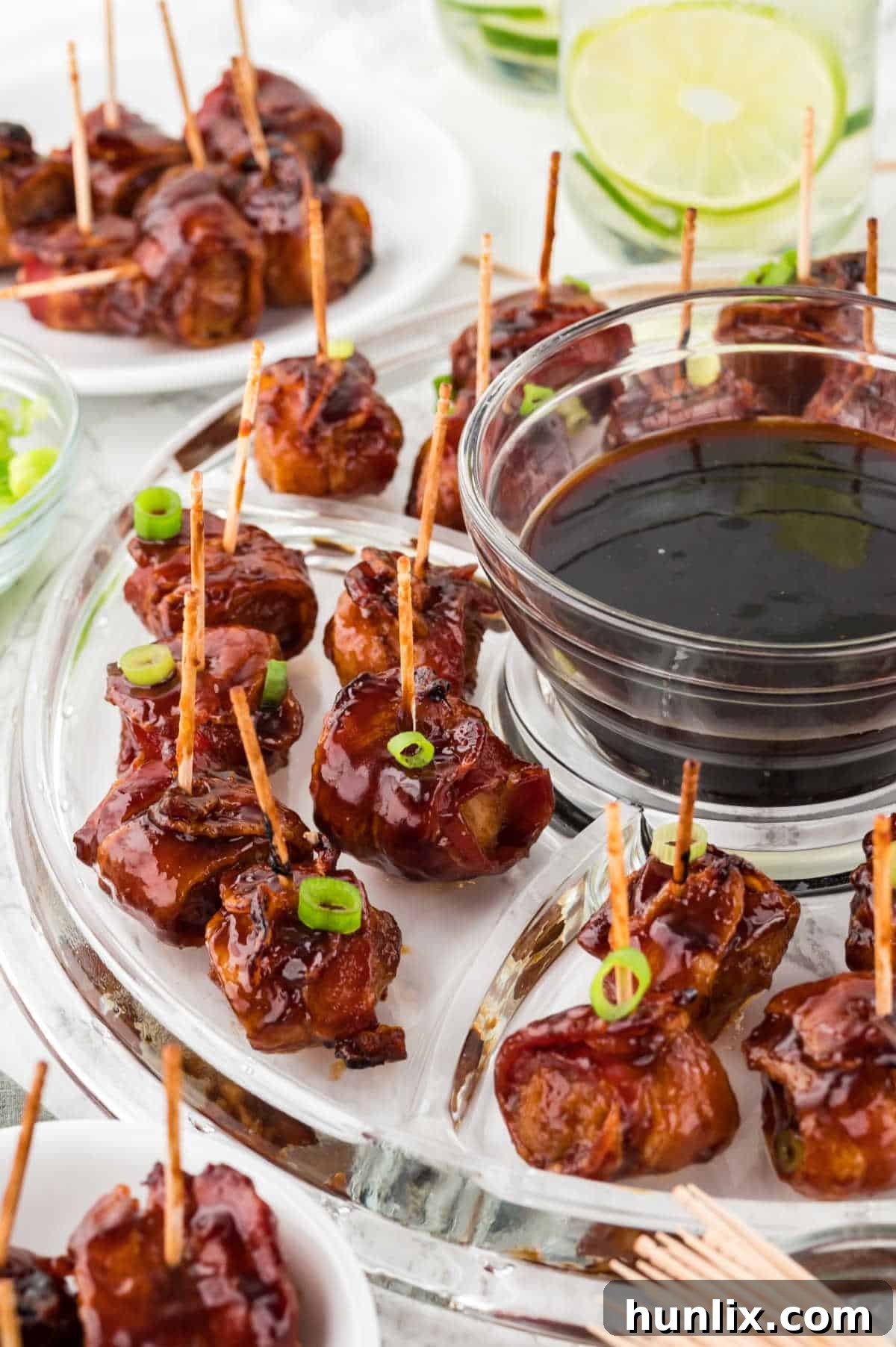 A vibrant serving platter of bacon wrapped water chestnuts, garnished beautifully, with a small bowl of extra dipping sauce on the side.