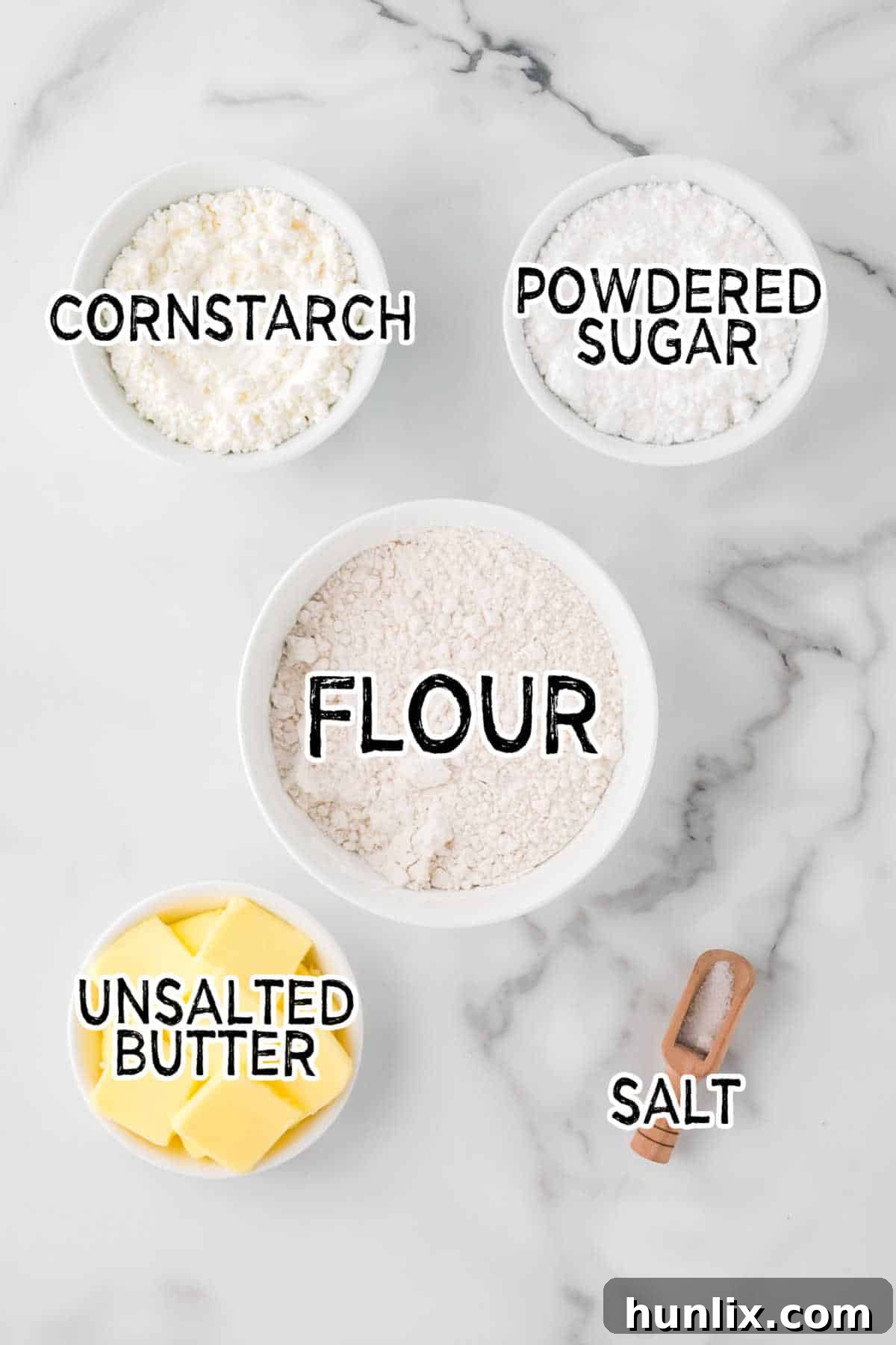 Ingredients for whipped shortbread cookies artfully arranged on a marbled counter, including butter, powdered sugar, flour, and cornstarch.