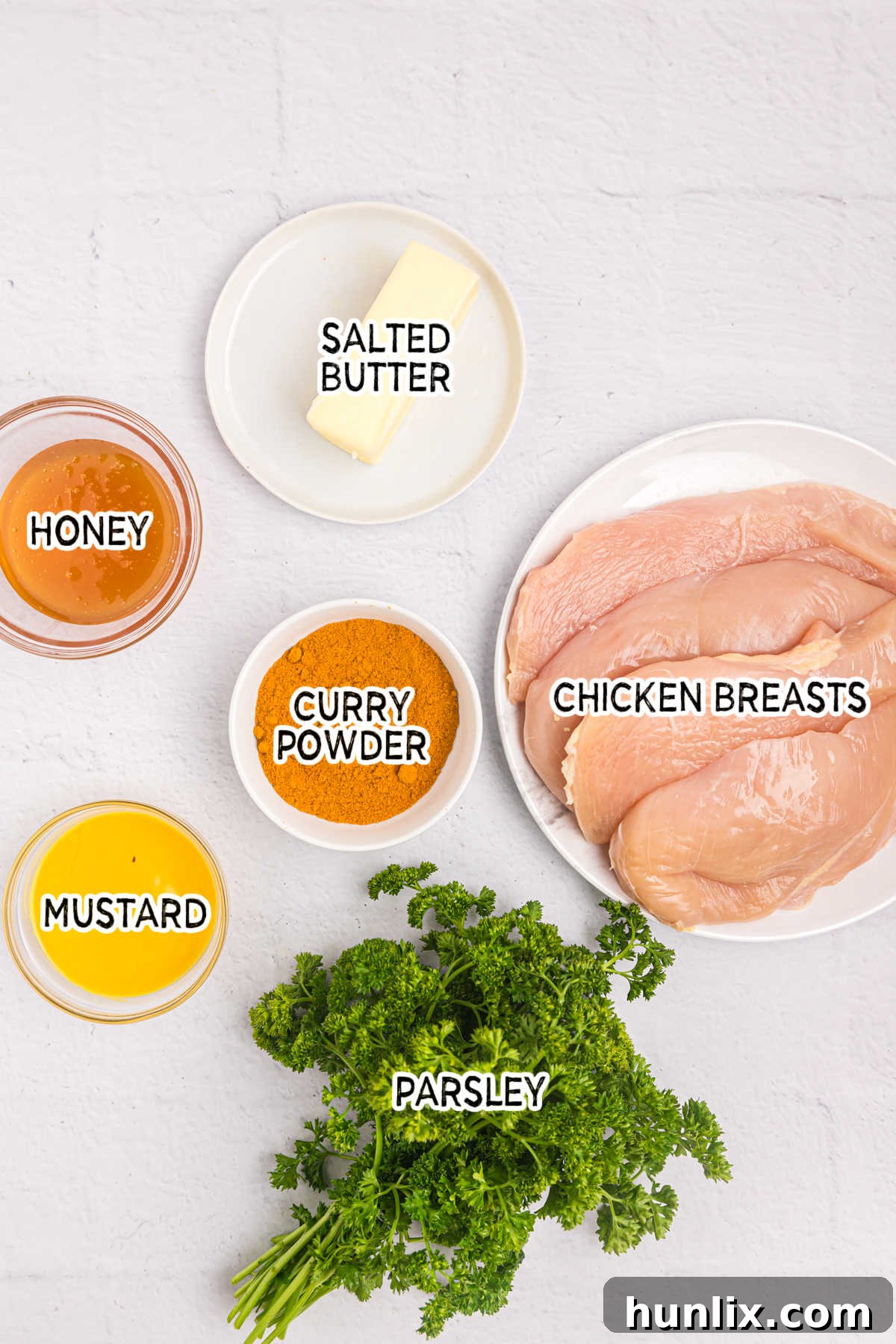 Fresh ingredients laid out: chicken breasts, honey, butter, mustard, curry powder, and parsley.