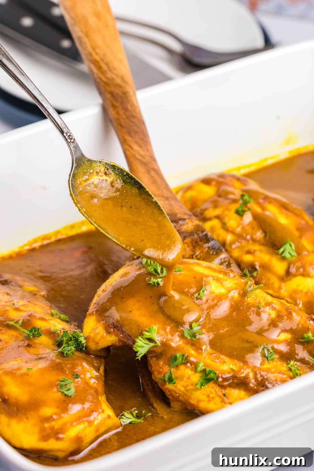 A close-up of a serving spoon drizzling honey curry sauce over a piece of cooked chicken in a pan.